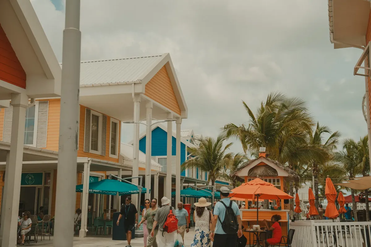 Tourists enjoy a colorful street lined with shops and palm trees on a sunny day.