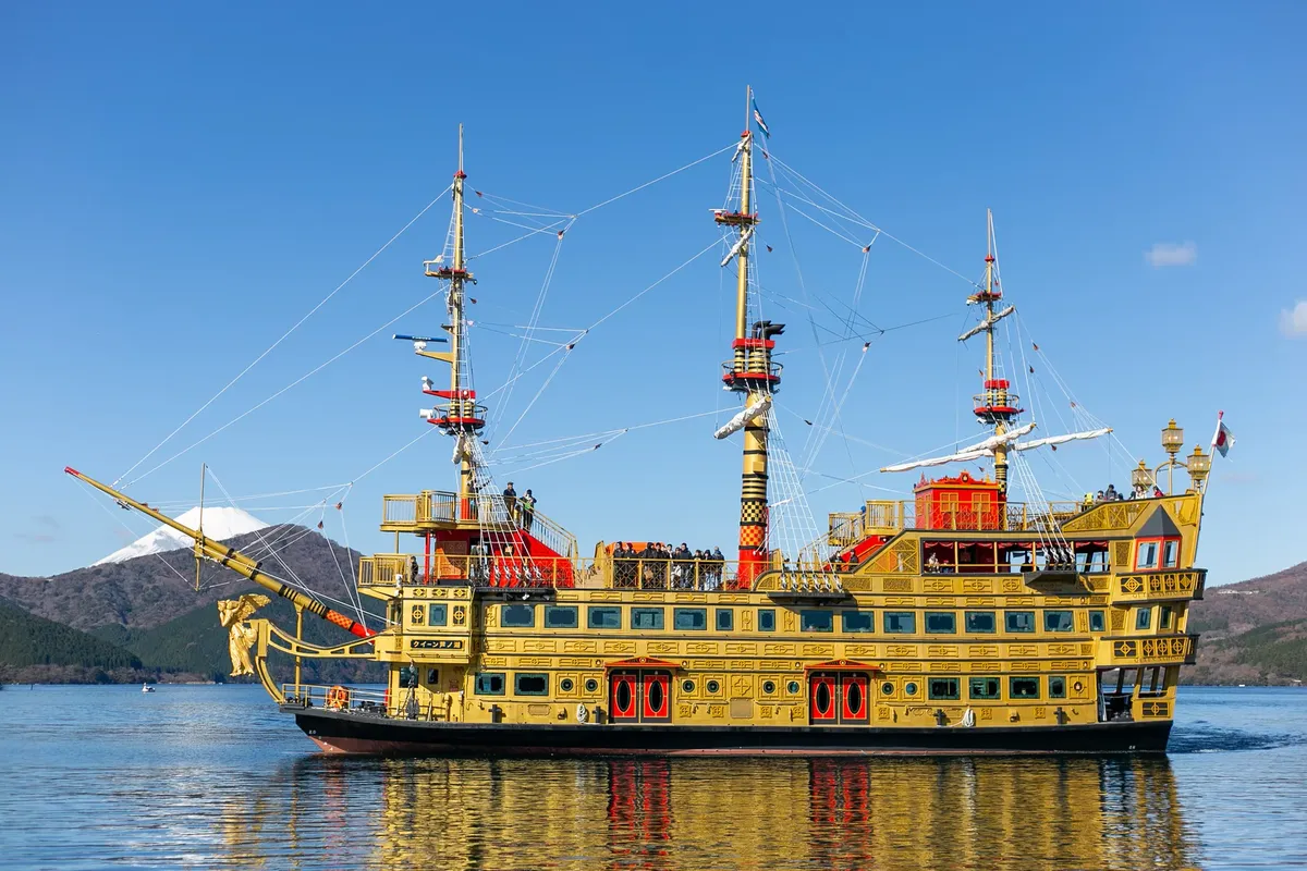 Colorful pirate ship sailing on Lake Ashi with snow-capped Mount Fuji in the background, under clear blue skies.